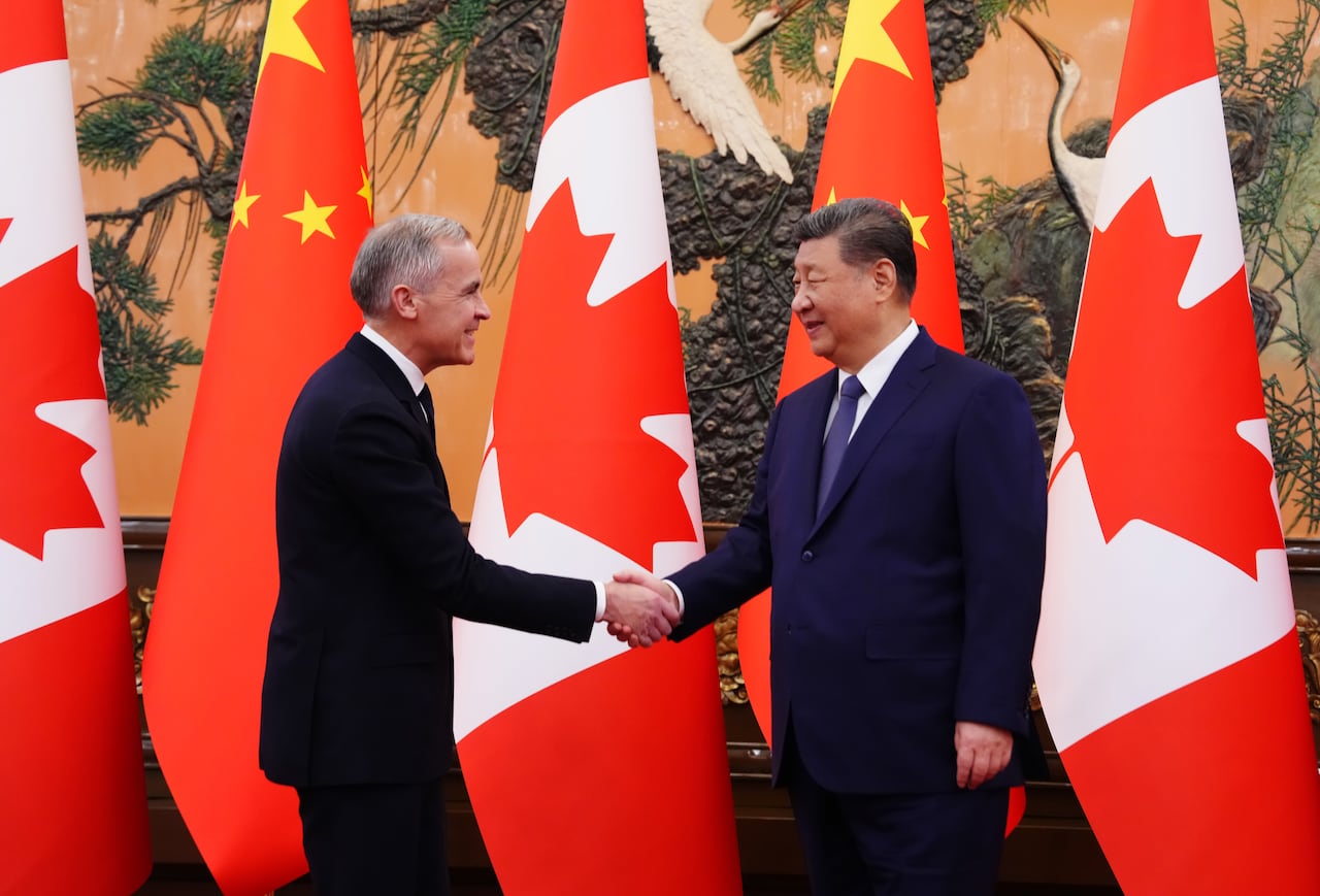 Two men in suits shake hands, flanked by Canadian and Chinese flags.