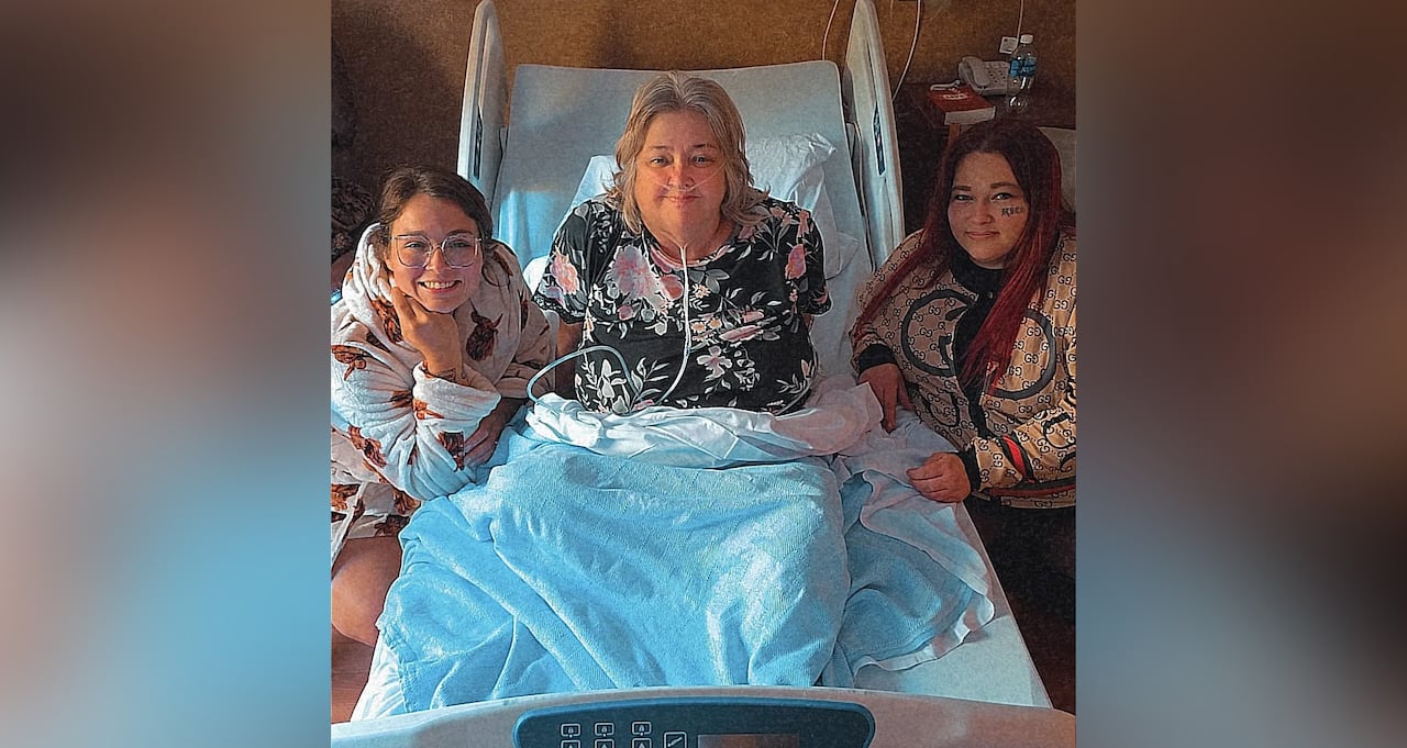 A woman in palliative care sitting on a hospital bed next to her granddaughters.