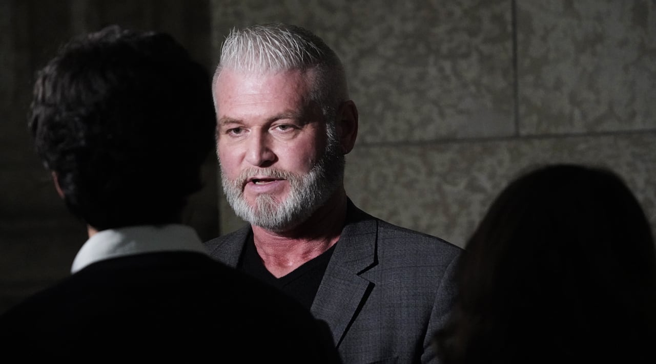 A man in a grey suit speaks to a reporter.