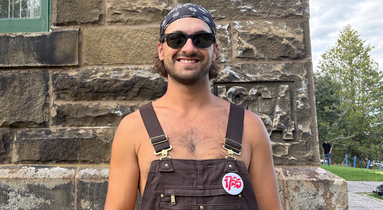 A smiling man wearing sunglasses and a black bandana. He is also wearing black overalls.