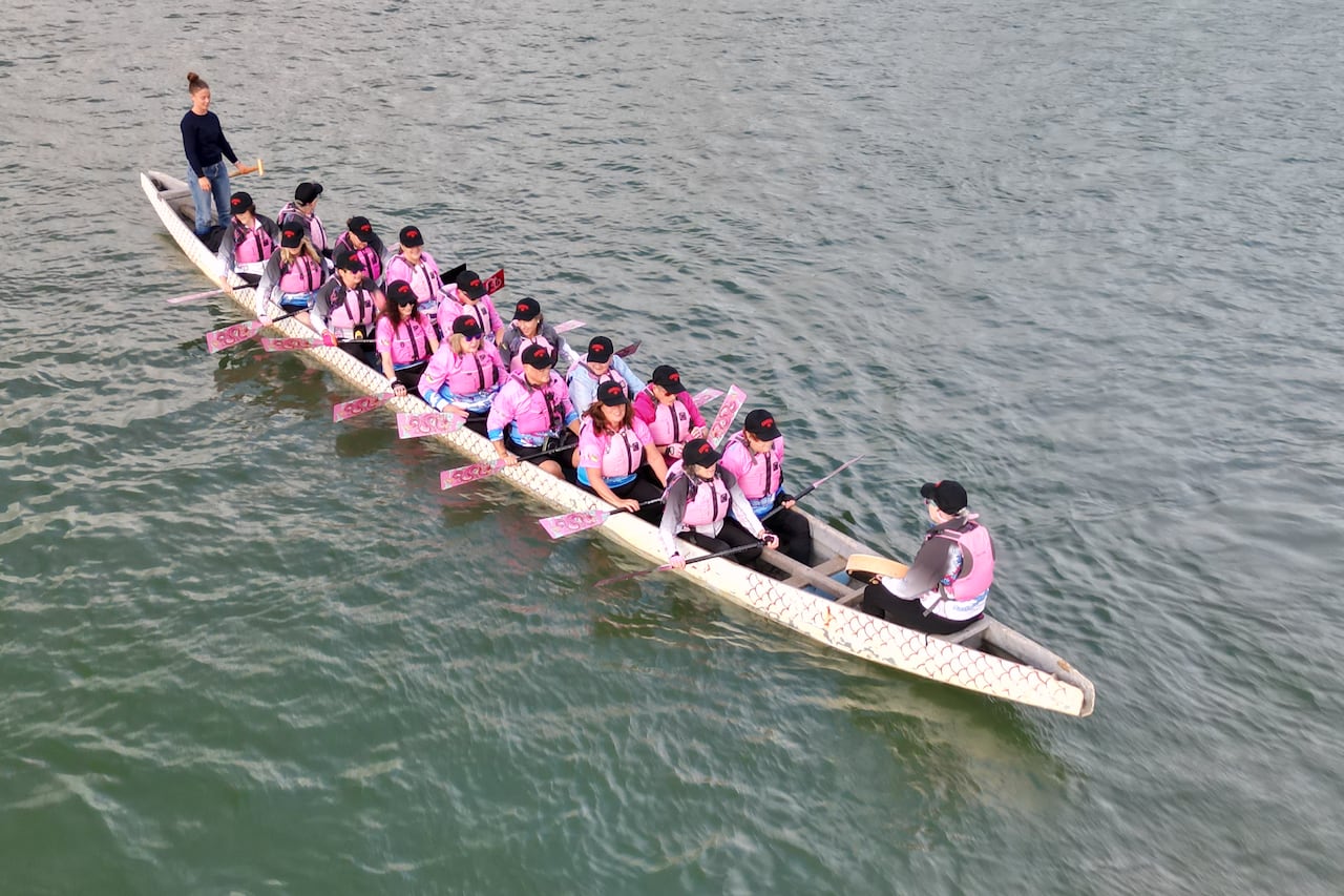 An aerial shot of women wearing pink sitting in a dragon boat on a river.