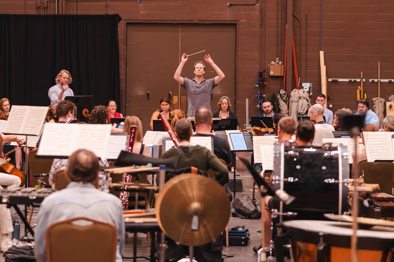 A view of a conductor with his arms in the air from behind the orchestra pit.