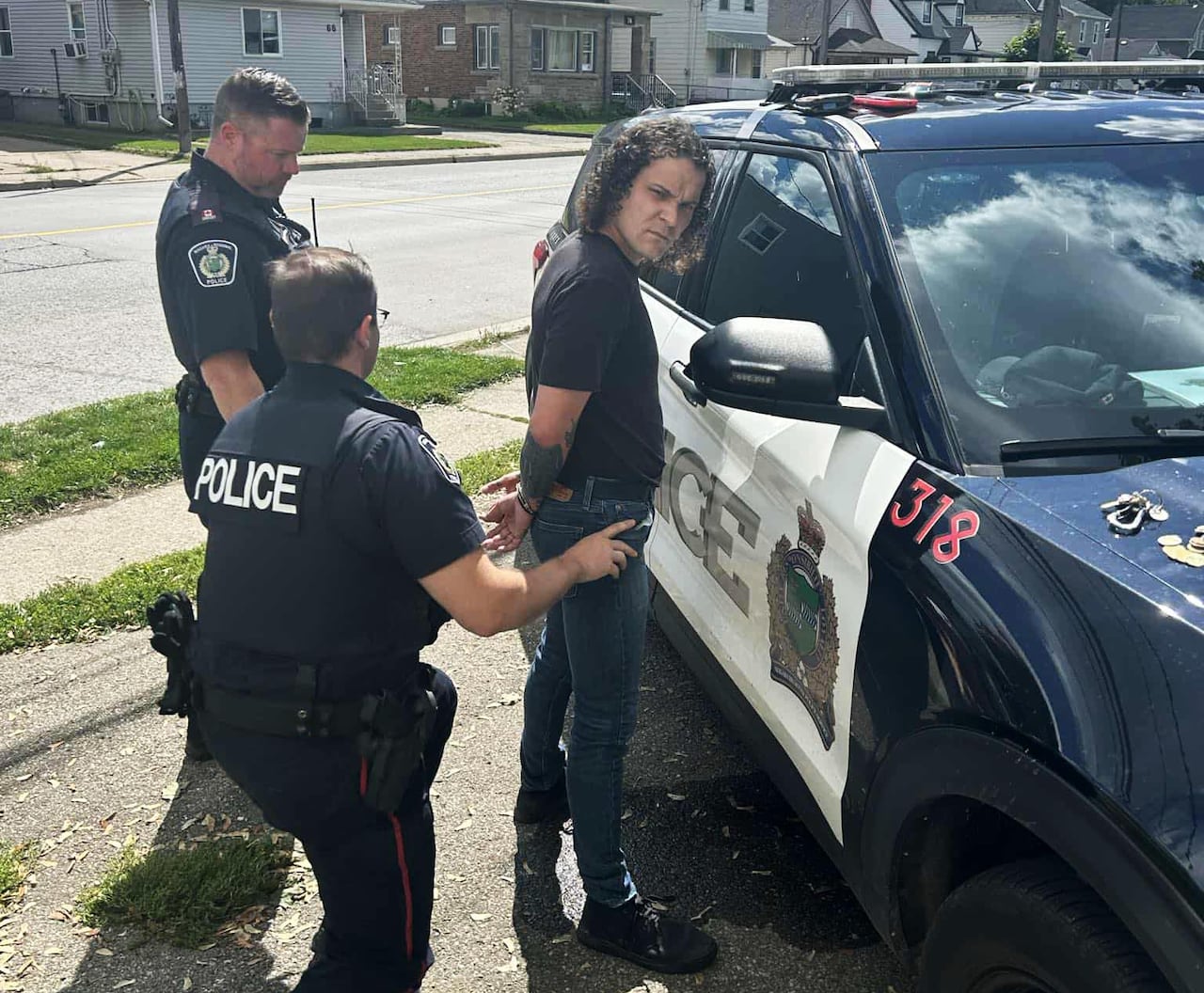 man being handcuffed a police car with two cops behind him