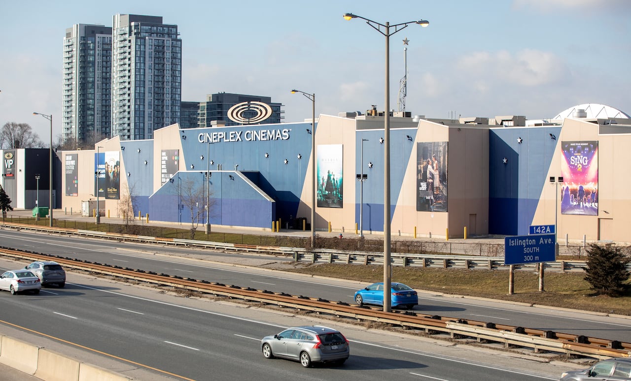 A highway is shown with a few cars on it, passing by a large building that says "Cineplex" on the side.