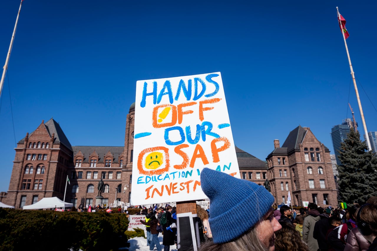 多伦多皇后公园立法大楼前的抗议人群，标语为 “Hands Off Our OSAP”