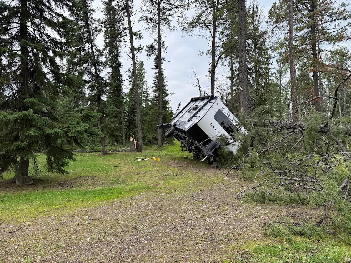 A tree is uprooted and has swept a mobile home up onto its side.