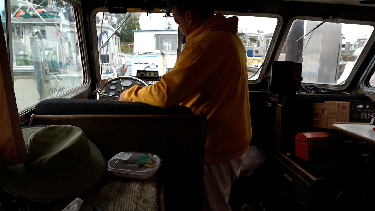 A man at the helm of a fishing boat in a harbour