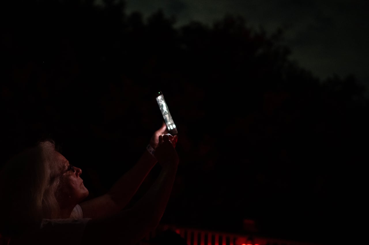 A woman holding up a cellphone towards the sky and the front shows a scene of a full moon.
