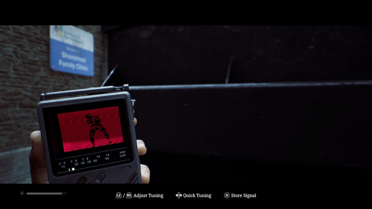 Video game screenshot of a person looking at a small handheld TV; a blurry shadow of a humanoid creature is seen on the fuzzy black and red screen.