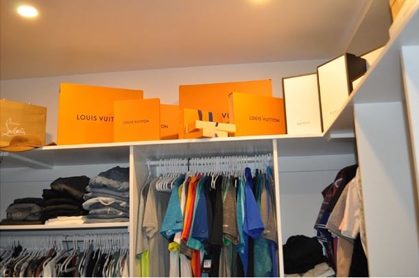 A closet with Louis Vuitton and Gucci bags and boxes on a shelf is shown
