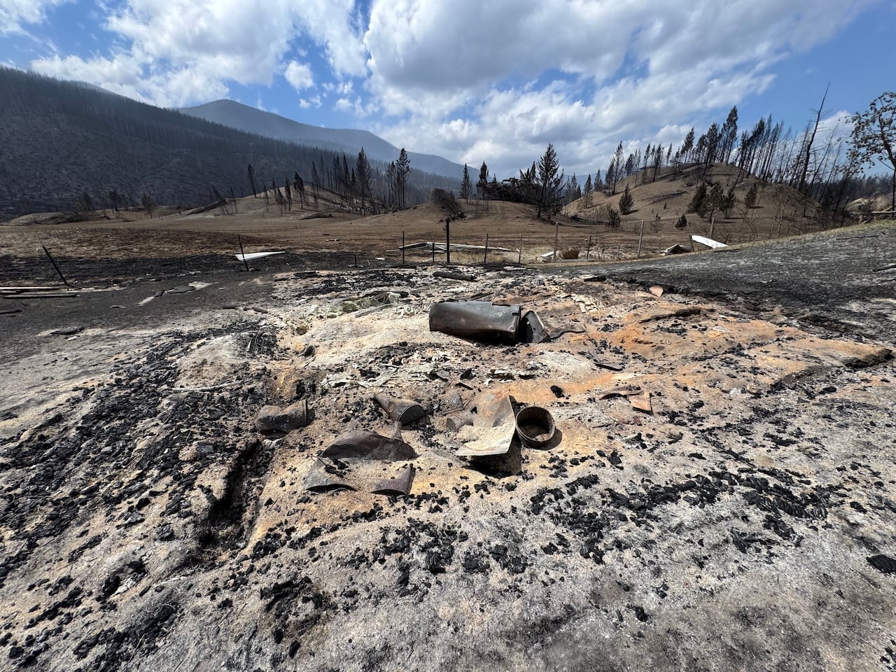 A scorched patch of earth where a home once stood. Little debris remains.