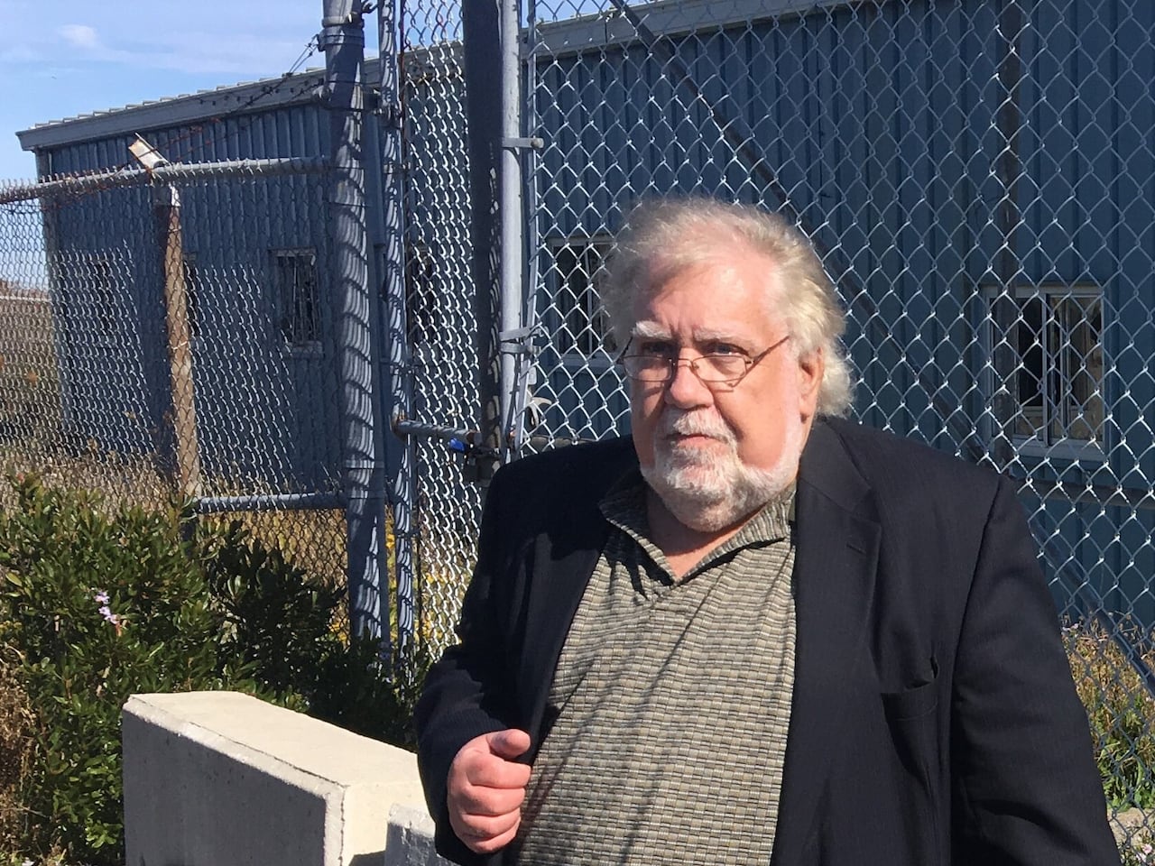 An author wearing a blazer poses for a photo outside of a chain fence.
