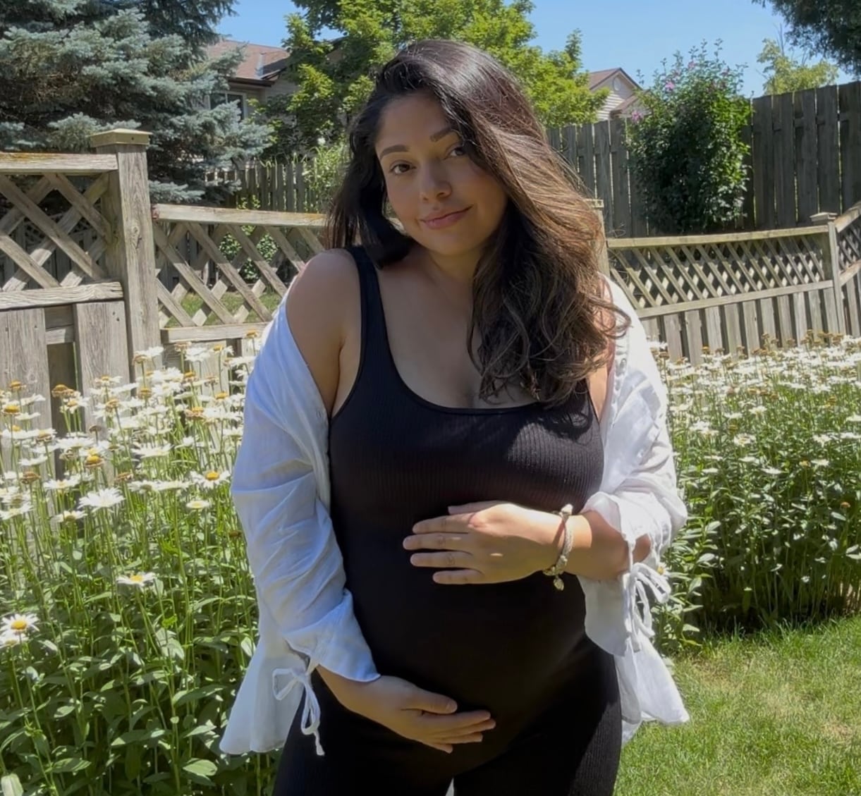 A pregnant woman holds onto her stomach while posing in her backyard