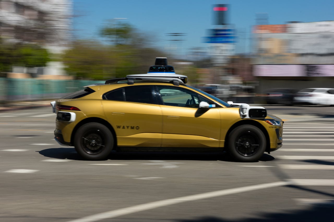 A gold painted Waymo driverless vehicle drives down a street in Los Angeles.