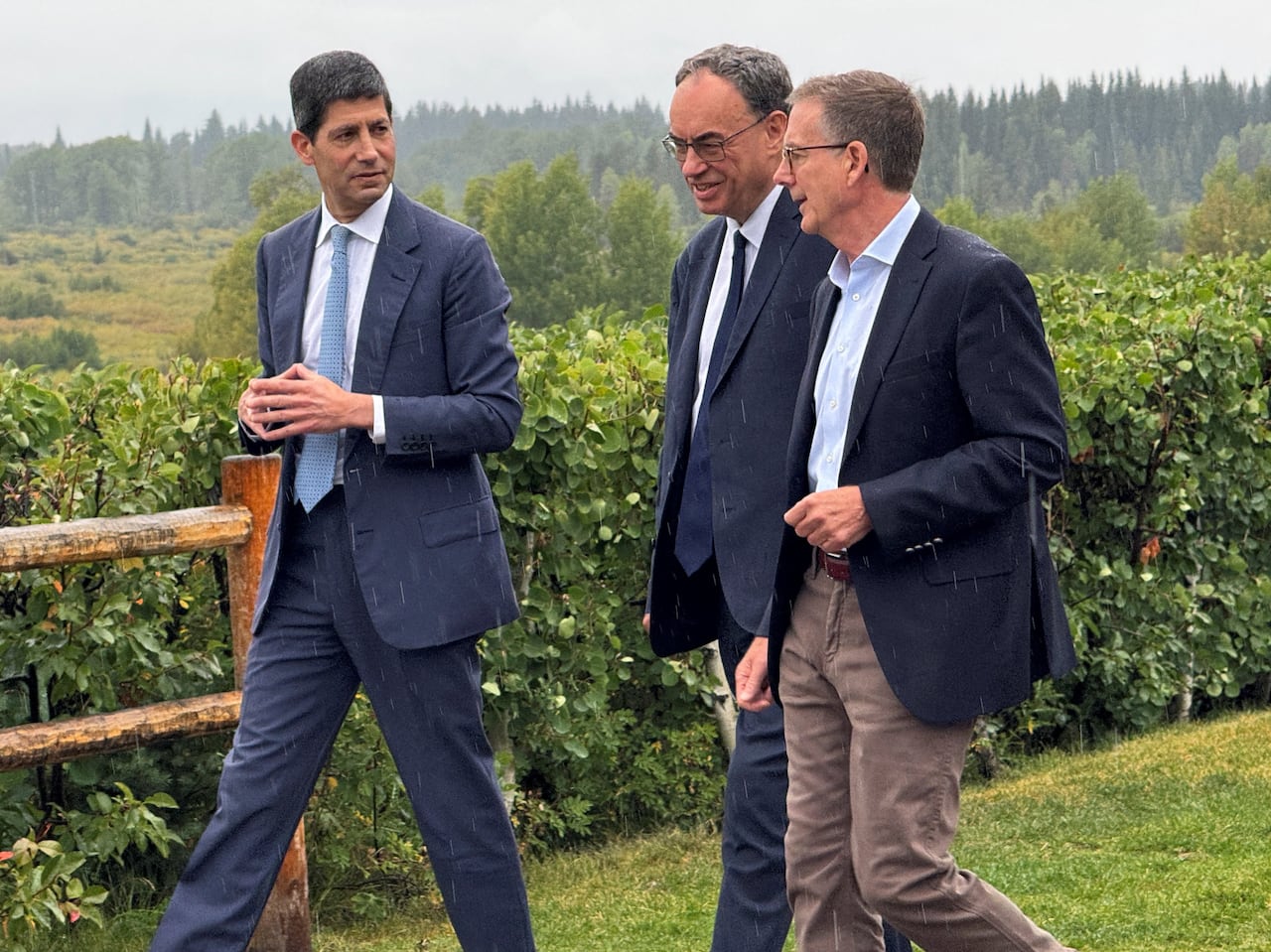 three older men in suits walk in a grassy area as light rain comes down