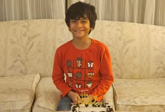 A little boy smiles behind a birthday cake.