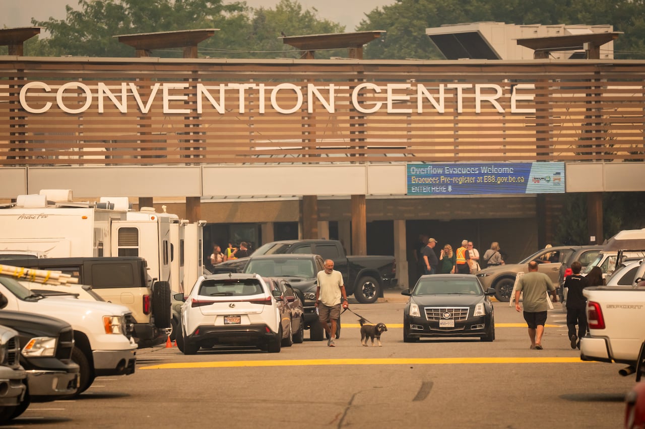 People in a full parking lot of a convention centre, amid hazy air.