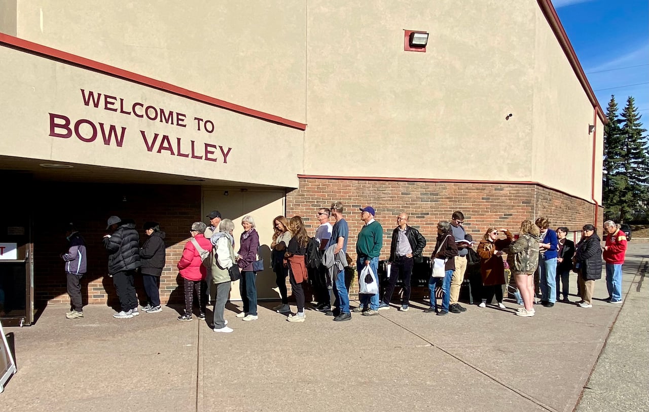 A lineup of people outside a building. Above the door is a sign for Bow Valley