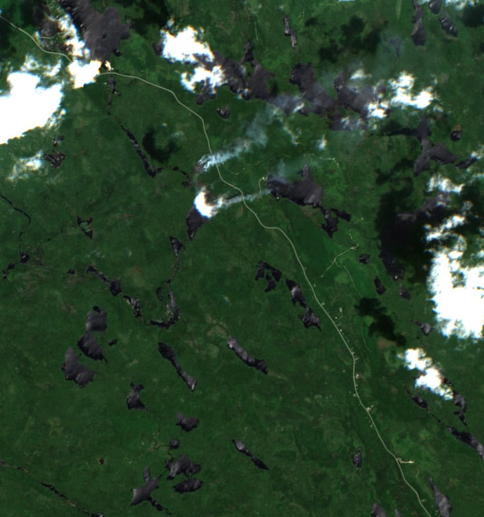 An aerial view of a forested area with some billowing above part of it.