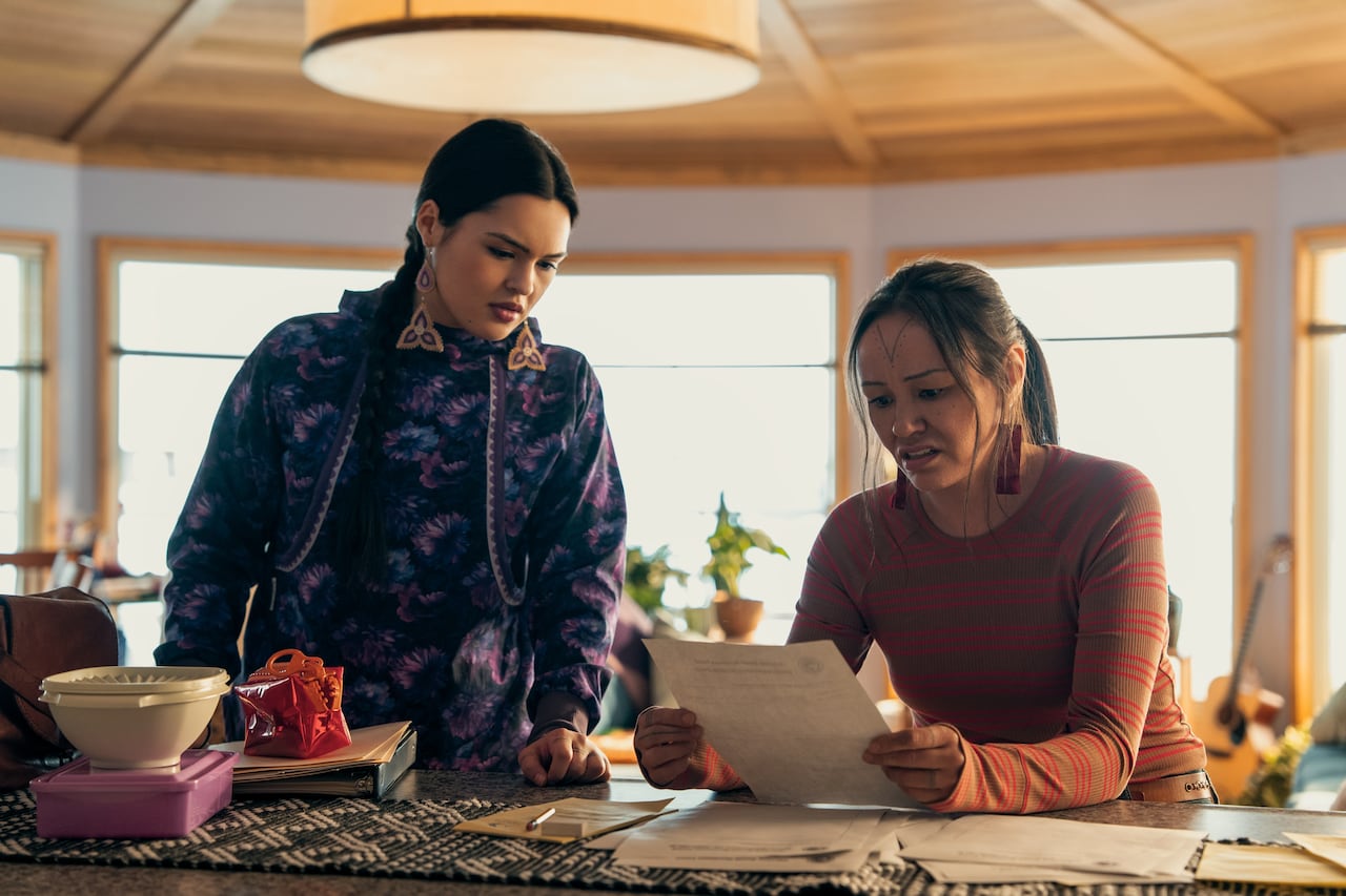 Two Indigenous woman look down at a piece of paper.