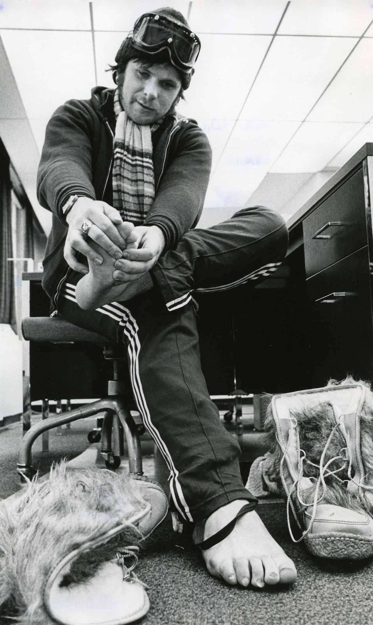 A black and white photo of a man rubbing his feet in what appears to be an office space.