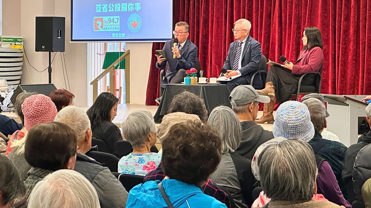 Three people sit on stage and speak to an audience.