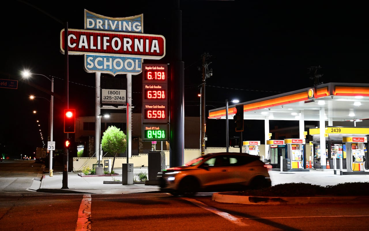 A gas station is shown at nighttime, with vehicles driving past it.