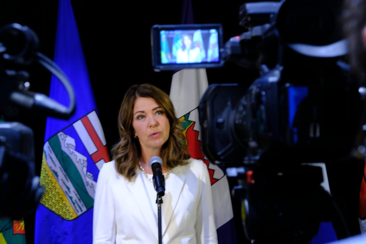 TV camera captures a politician talking in front of flags.