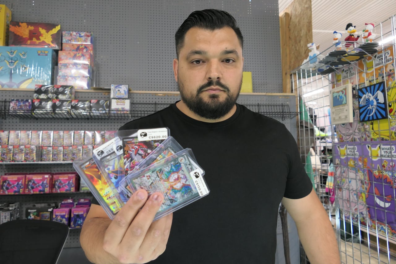The man holding up a set of cards in front the empty shelves that his product was stolen from.