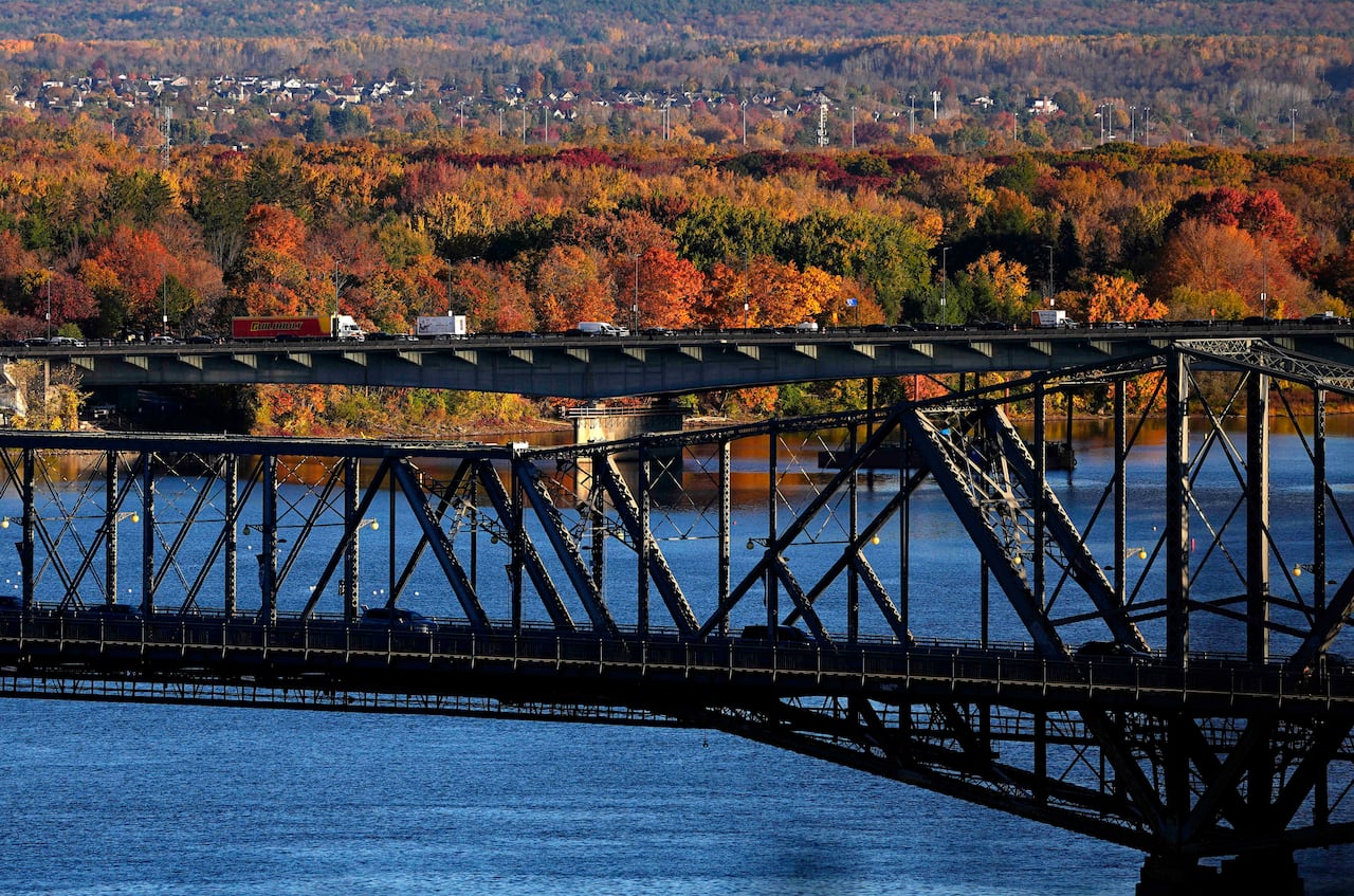 A brdige over a river with trees showing foliage in the distance.