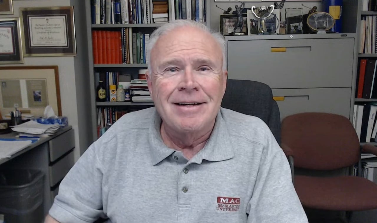 A man in a grey shirt smiles into the camera.