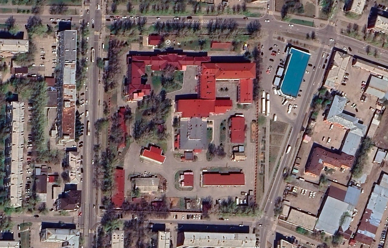 A satellite image of a complex of buildings with clay red rooftops, surrounded by paved roads and other houses and buildings.
