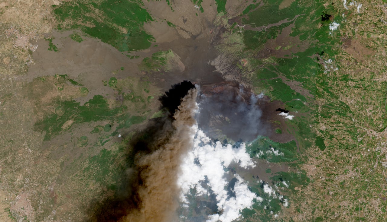 A satellite view of an active volcano with its plume of dark smoke.