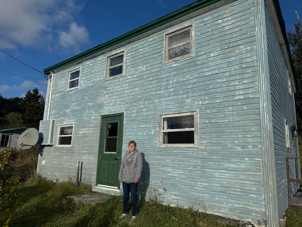 A woman stands in front of a home with blue siding, edged in white paint to look distressed.