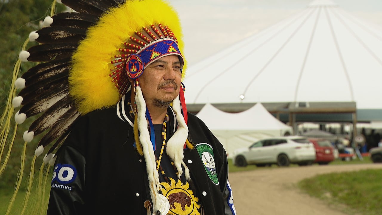 First Nations man wearing a headdress with yellow feathers. He is also wearing a beaded medallion with an image of a buffalo.