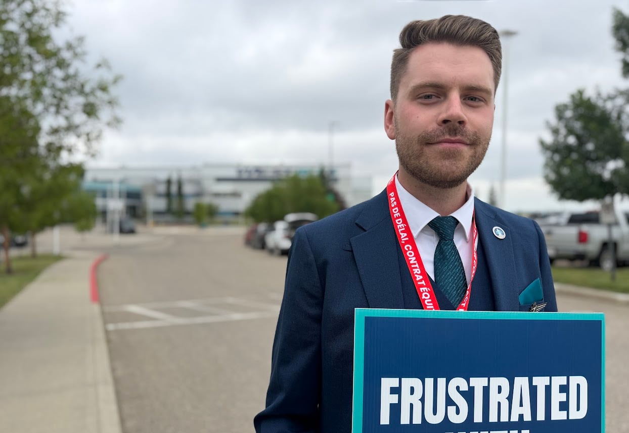 A man in a flight attendant's uniform stands outside a WestJet building with a picket sign saying "frustrated"