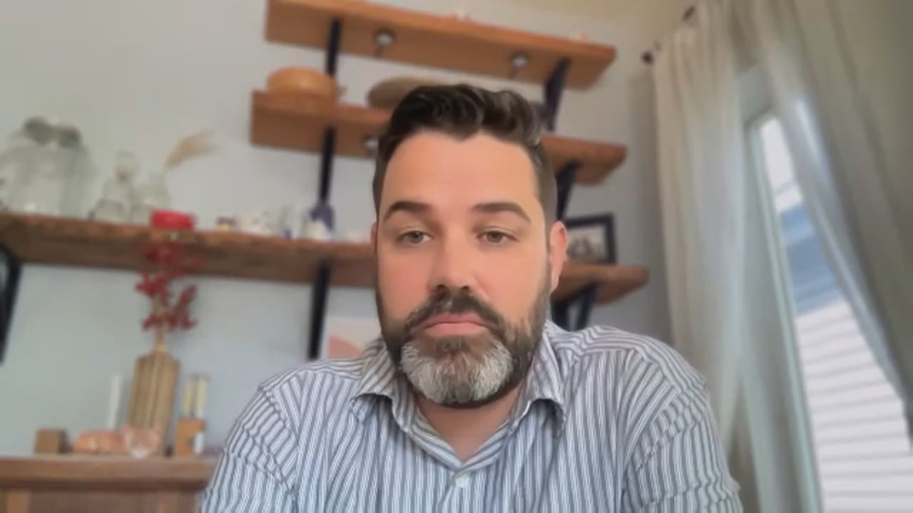 一位棕发留着花白胡须的男士穿蓝白条纹衬衫在家中
