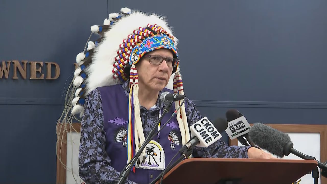 A man with a traditional headpiece stands at a microphone.