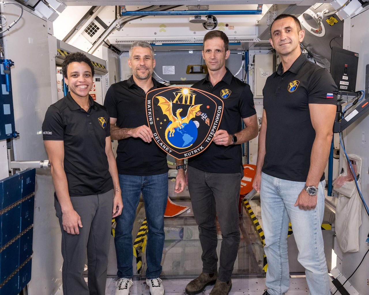 Four people hold up a large patch.