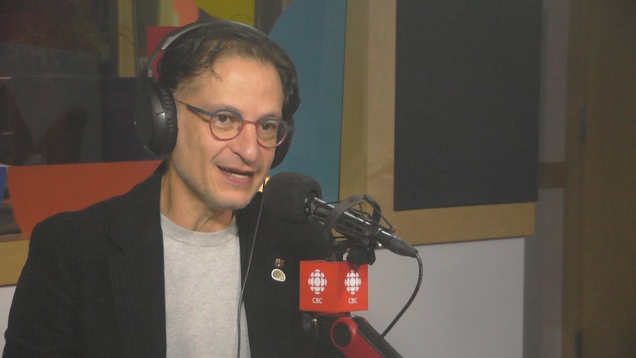 A man with rounded glasses speaks in a radio studio.