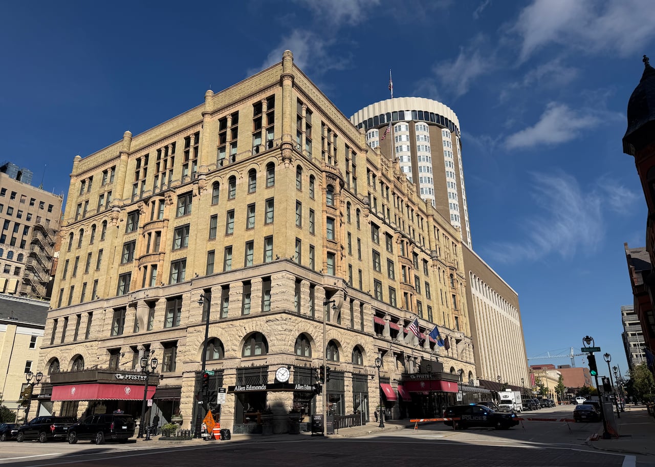 Two facades of a historic hotel made of beige brick with an adjoining tower.