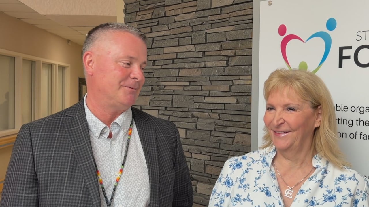 A man and a woman share a laugh while talking to reporters at an event in a hospital meeting area.