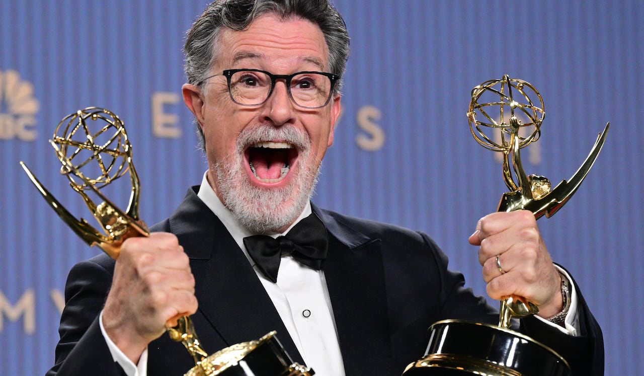 Man holds two Emmy Award statues as he smiles for camera.