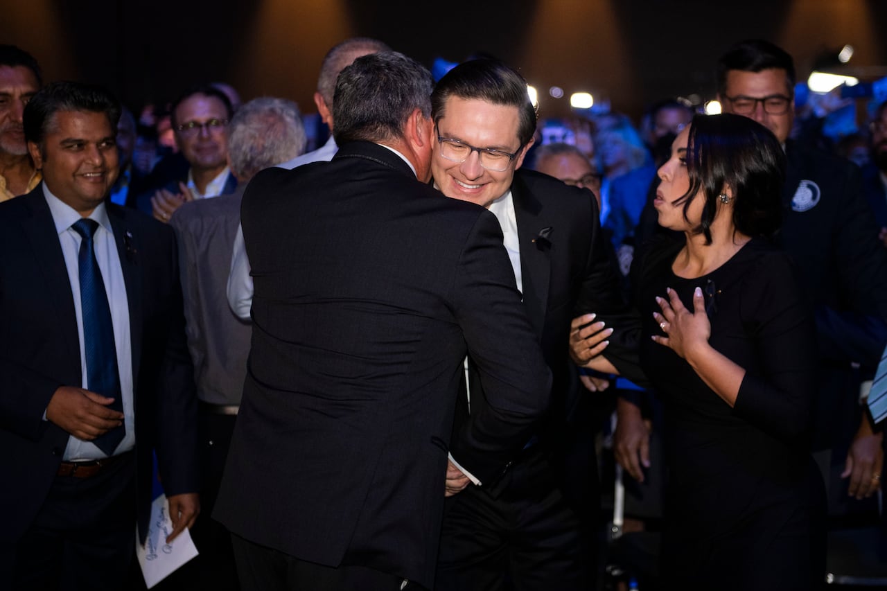 Two men in suits shake hands and hug.