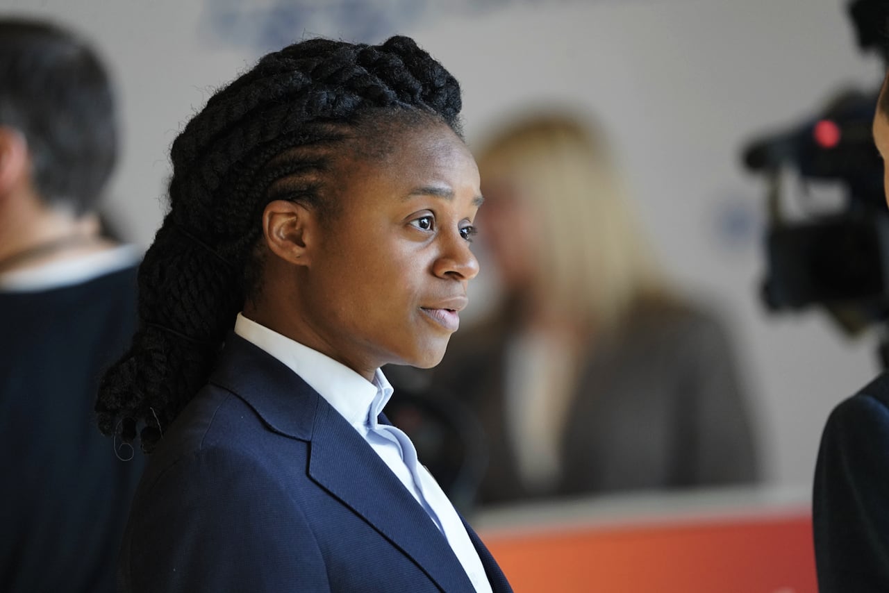 A person in a dark blue suit speaks with someone outside the frame.