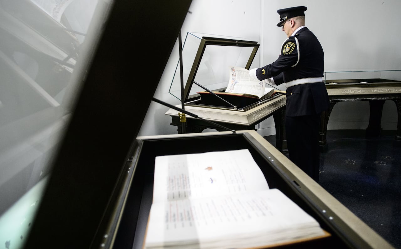 A man in a uniform stands over a book housed in a glass case.