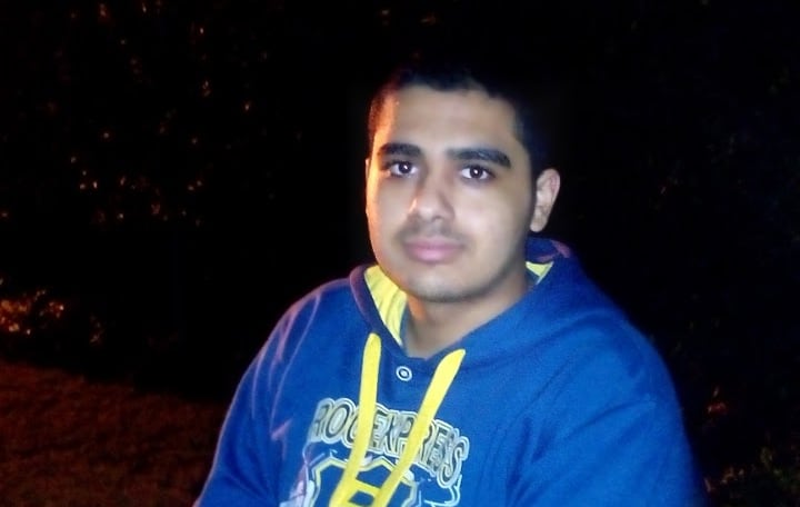 A photo at night with a youth sitting in a chair wearing a blue hoodie with yellow hoodie strings.