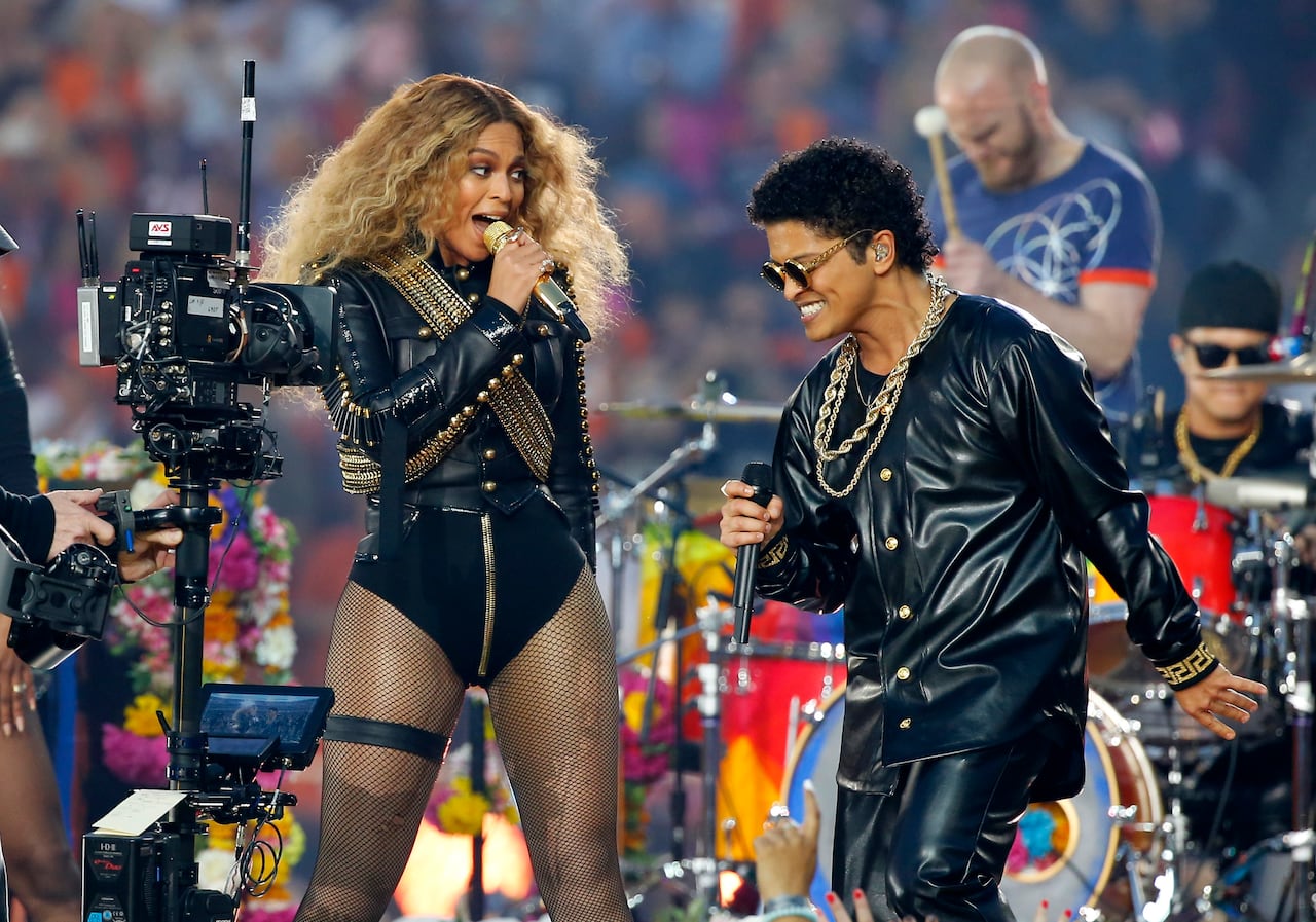 Two performs in black singing into mics and dancing
