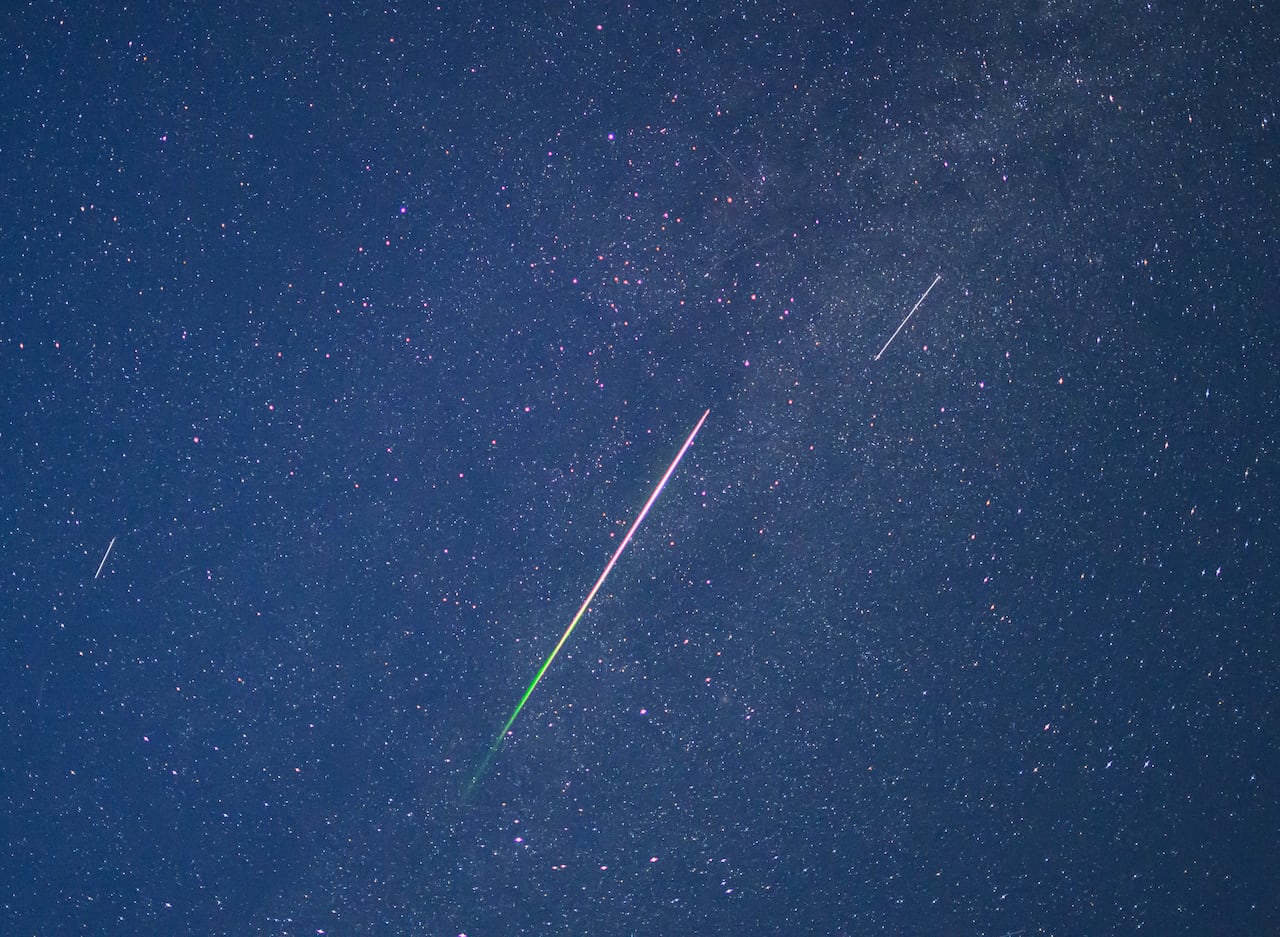 Closeup of meteor streaks and stars in the sky at night.