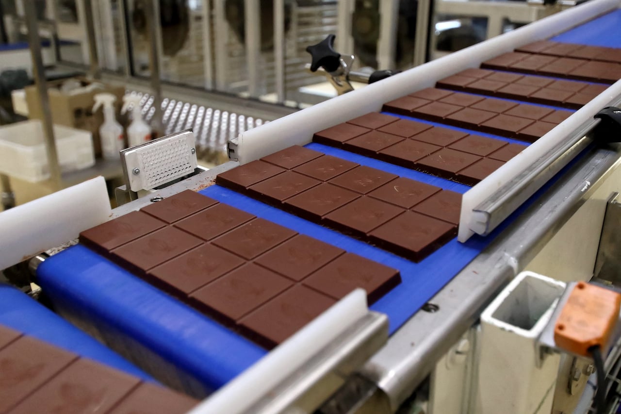 Chocolate bars sit spaced on a blue conveyor belt in a production facility.